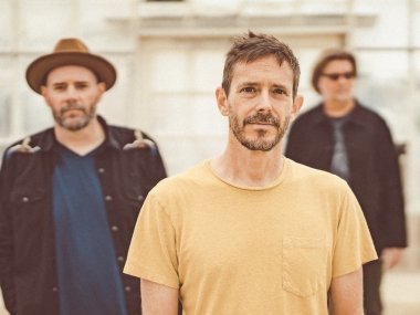 Three men stand facing the camera. The one in front is in focus, and the two slightly behind are blurrier.