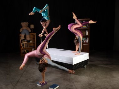 Three acrobats posed in different variations of handstands on stage.