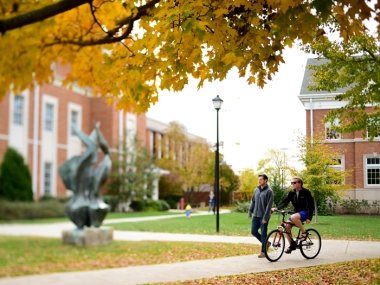 one student walking and one on a bike near the flame statue