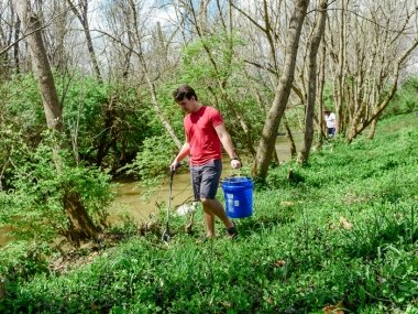 Student picking up trash along bank and putting it in bucket