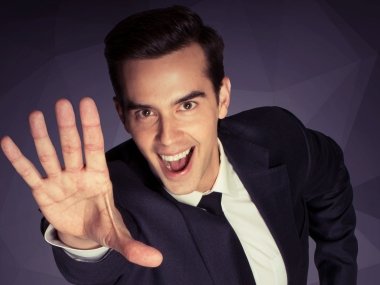 Michael Carbonaro holds his hand up to the camera and smiles widely