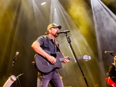 Rodney Atkins stands on stage with stage lights shining down behind him. He is singing into the microphone and playing guitar.
