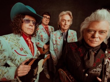 Marty Stuart and his band members pose against a black background with a wide distorted angle