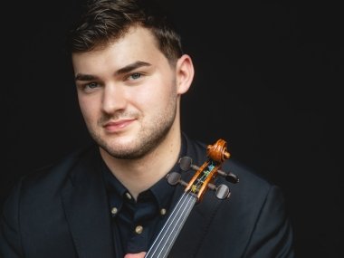 Nathan Metlzer headshot against a black background, with his violin resting against his shoulder