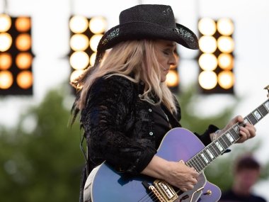 Melissa Etheridge performing a show, playing guitar with a cowboy hat on