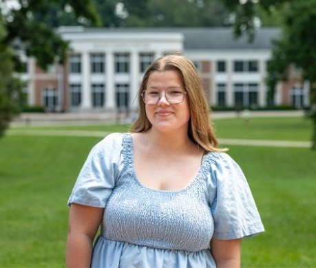 Student wearing dress standing outside with Roush Student Centre in background