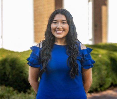 Student wearing royal blue dress standing outside of Old Centre and smiling at camera