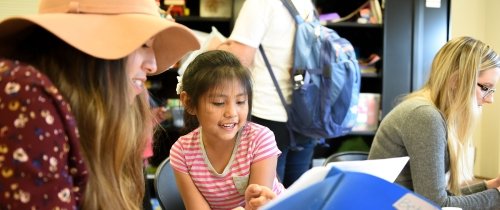 Student teaching a young girl in an after school program