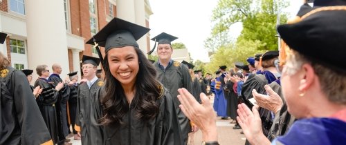 Students walking through lineup on graduation day in cap and gown being cheered on by professors