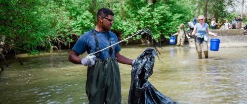 A student stands in a river doing trash clean up