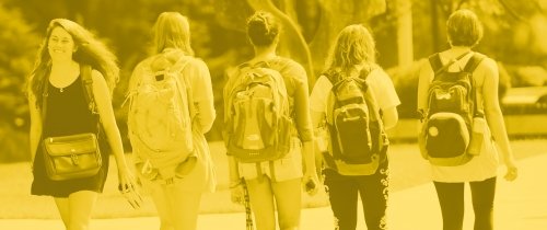 Student walking on campus wearing backpacks with gold tone