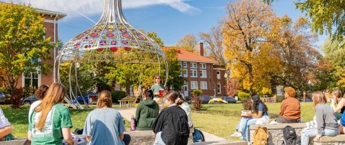 students sitting outside in outdoor classroom facing Stephen Powell memorial