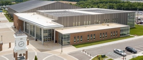 A large building is seen from above with solar panels on the roof and a bell tower is seen in the foreground.