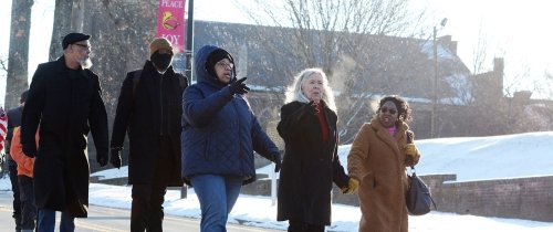 Three women lead a larger group marching along a downtown street.
