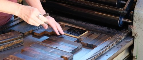 Two hands place panels on an old-fashioned letterpress printing press.