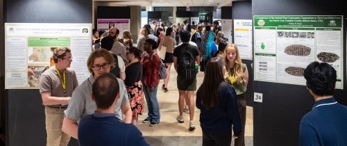 A hallway is filled with people talking with one another in front of research posters mounted along the length of the hallway.