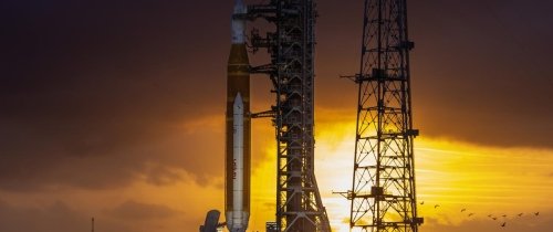 The Artemis II rocket is seen on the launch pad prior to blasting off into space with the sun setting behind it.