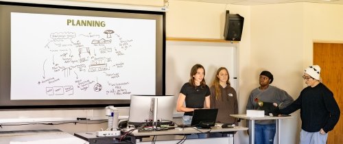 Four students stand in front of a classroom presenting