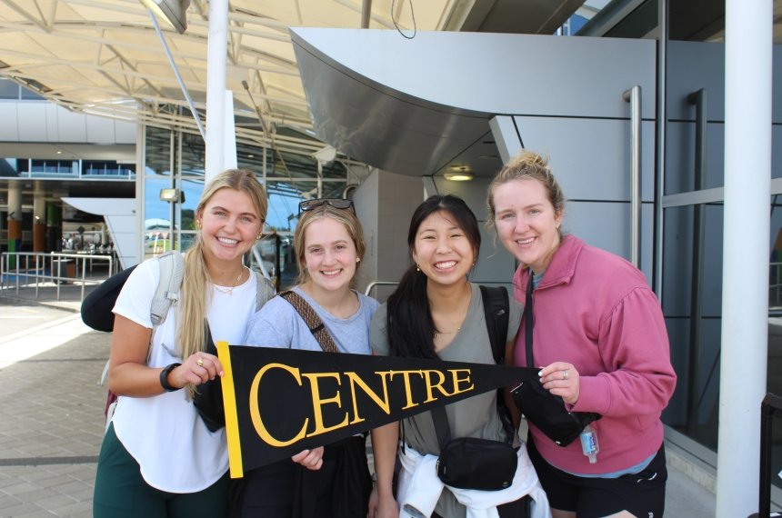 Four students hold a Centre College pennant while posing for a photo.