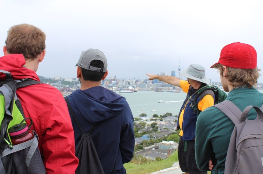 A professor points as he and three students look across a harbor.