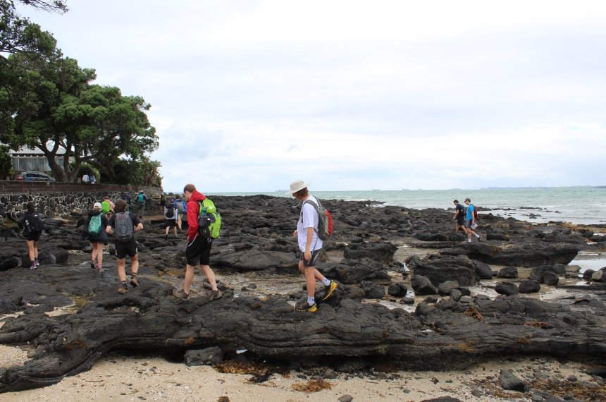 A line of students hike along a coastline lava flow.