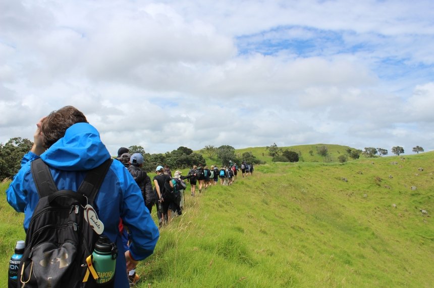 A line of students hike along a green grassy ridge.