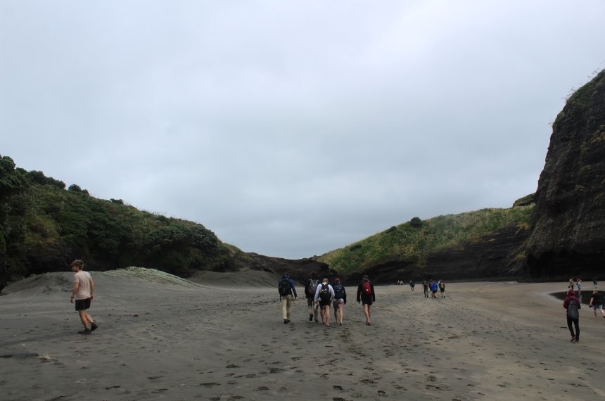 Students walk along a black sandy beach.