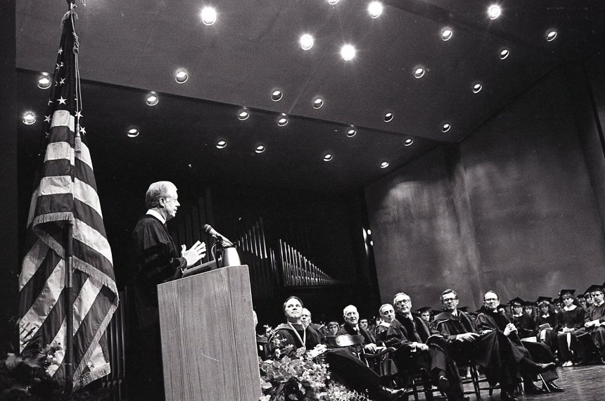 A U.S. flag stands behind Jimmy Carter as he speaks at a podium in front of an audience of Centre College faculty, staff and students.