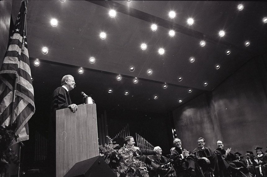 A U.S. flag stands behind Jimmy Carter as he speaks at a podium in front of an audience of Centre College faculty, staff and students.