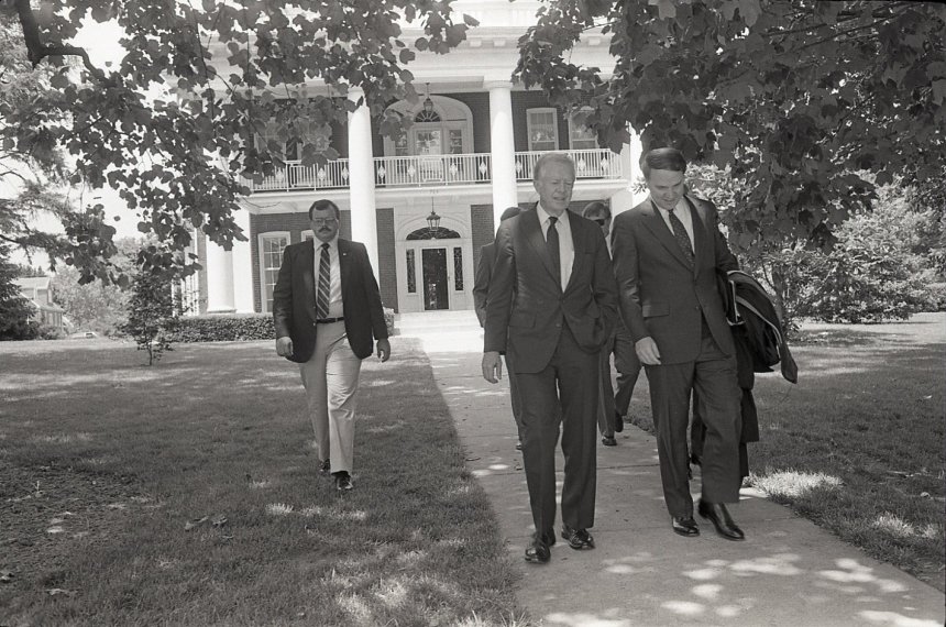 Centre College President Richard Morrill and former President Jimmy Carter, lead a group walking on a sidewalk under a tree with Old Centre in the background.