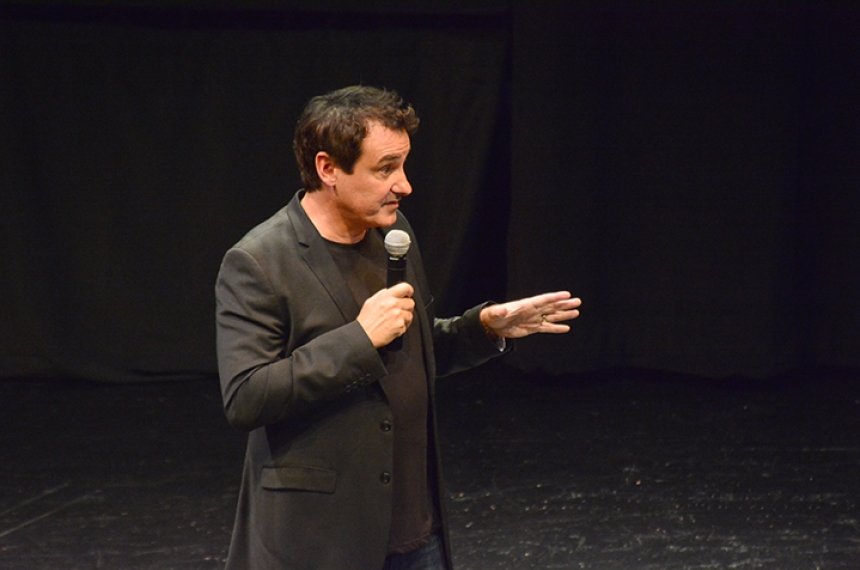 A man speaks into a microphone on a dark stage.