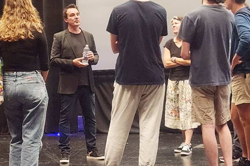 Students stand in a loose circle to listen to a man talk.