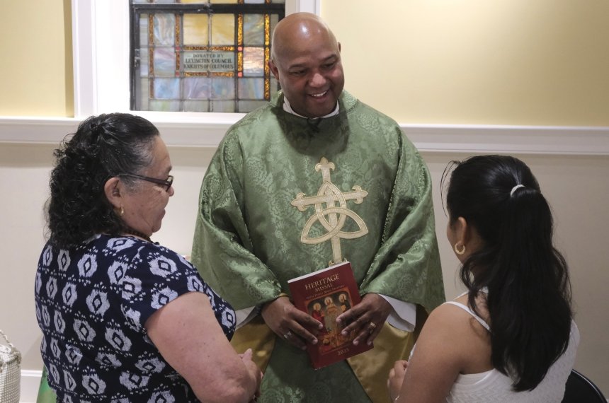 A priest wearing green and gold robes speaks with a young girl and a woman following the conclusion of a service.