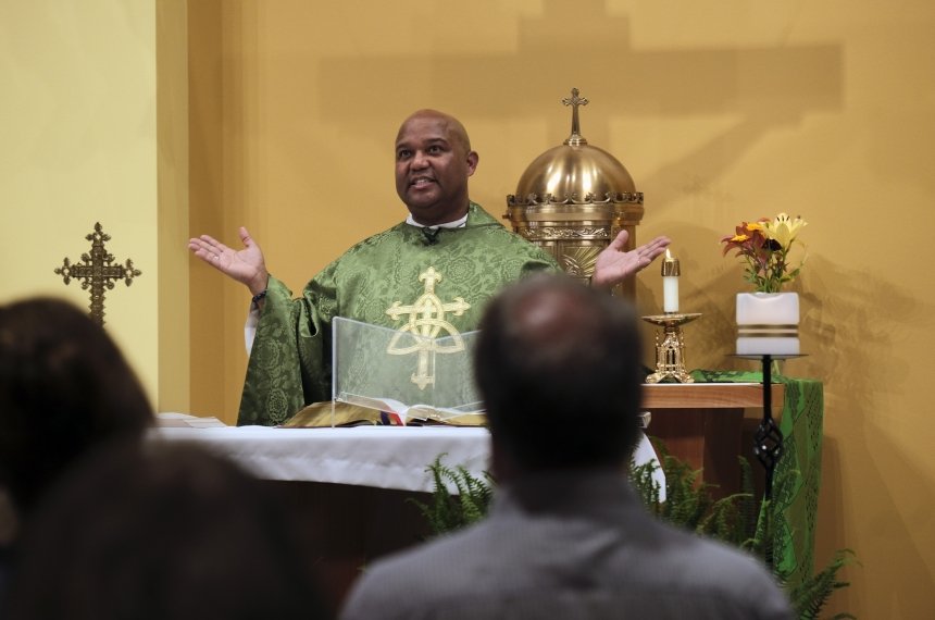 A man standing behind a lectern holds out his hands while saying a prayer during a religious service.