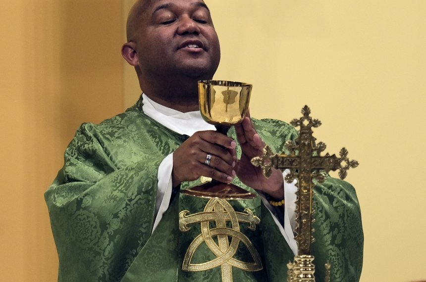A man in green and gold robes holds a golden goblet during a service.