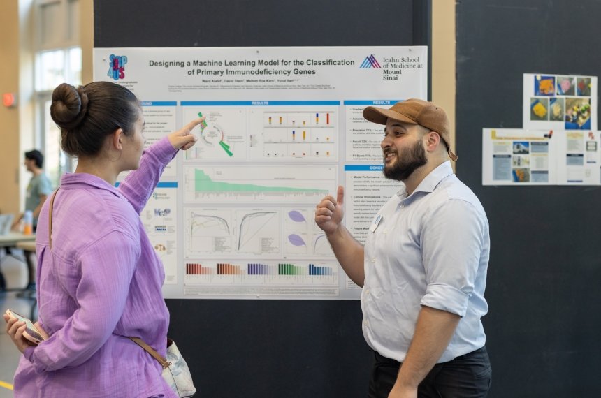 A woman points as a chart hanging on a display panel as she asks a young man about his internship experiences.