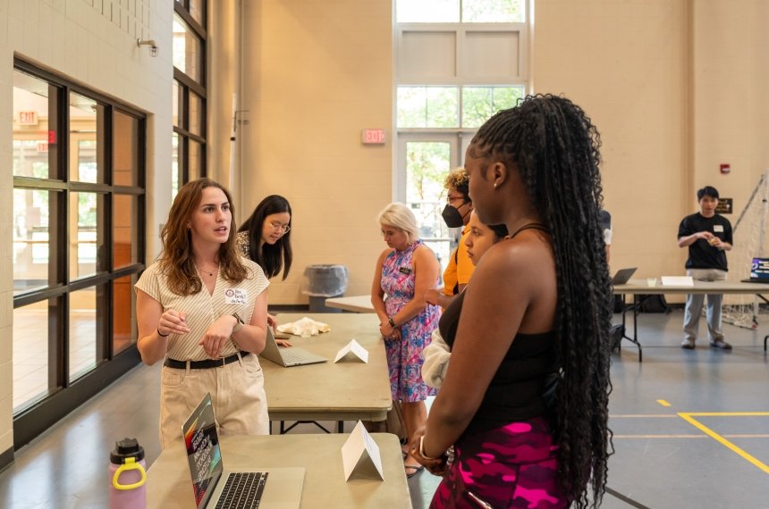 A young woman talks with another student across a table.