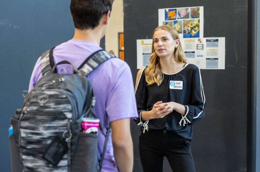 A young man stands with his back to the camera as he talks with young woman.