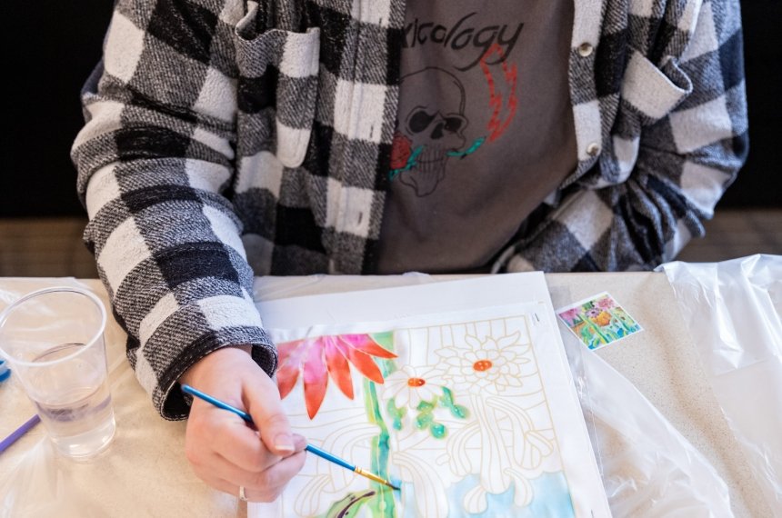A student adds paint to a painting of a flower.