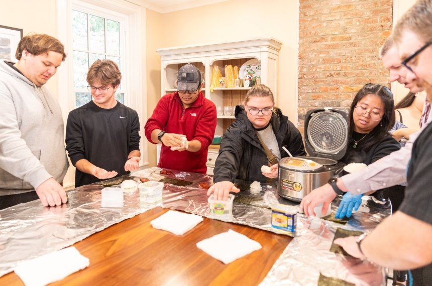 Students work on creating musubis while gathered around a large kitchen island.