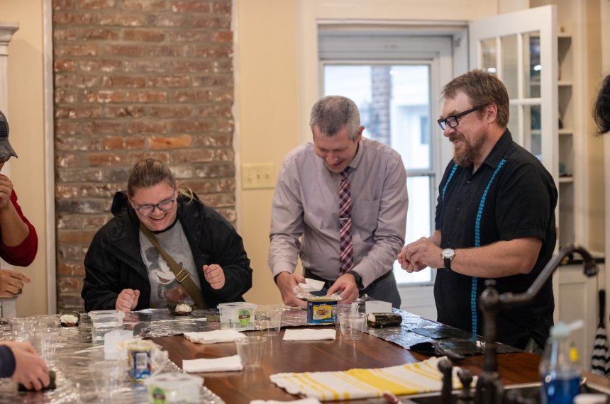 A woman laughs as she and two men work around a kitchen island.