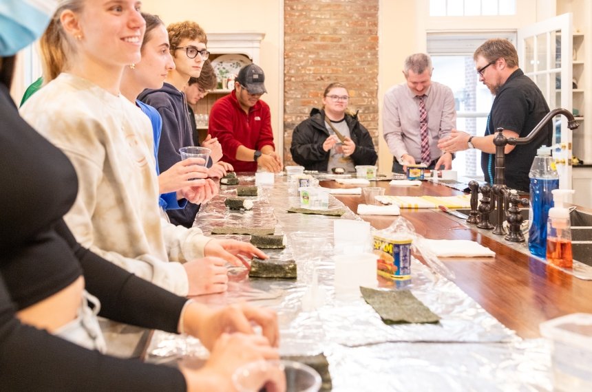 Pieces of foil cover the top of a kitchen island as students roll up musubis.