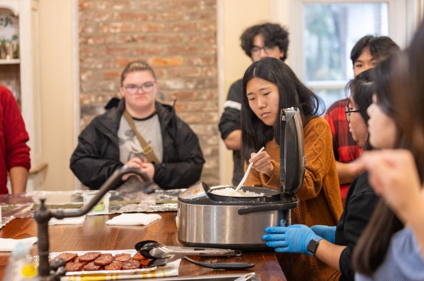 Students watch as a woman spoons rice out of a cooker.
