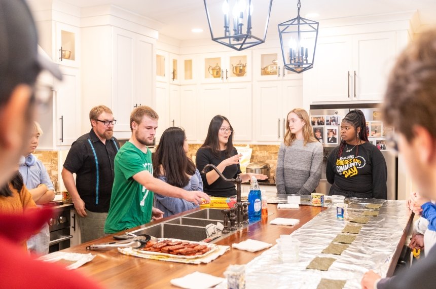 Pieces of foil cover the top of a kitchen island as students roll up musubis.