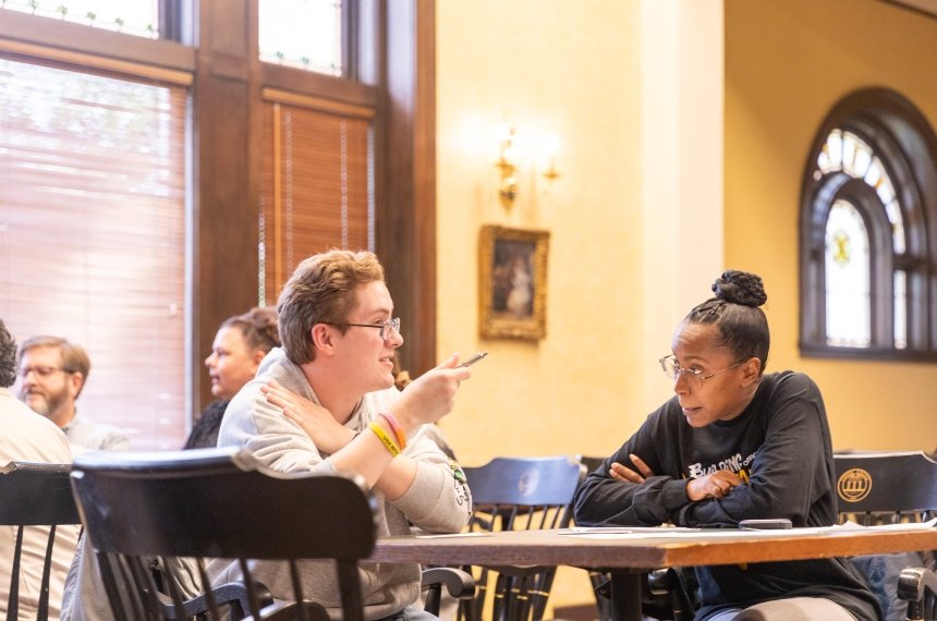 A man and woman seated at a small table talk.