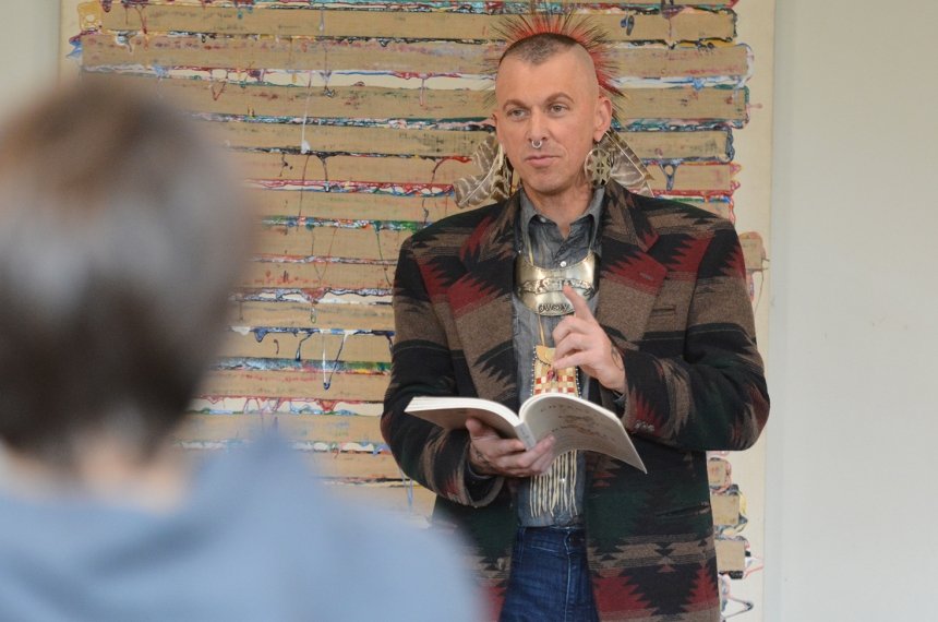 A man dressed in Native American garb addresses others.