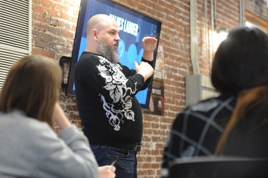 A man holds his hands several inches apart as he addresses seated students.