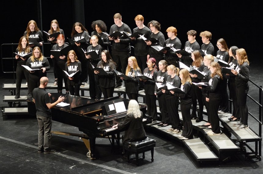 A choir stands on risers on the stage of the Norton Center for the Arts.