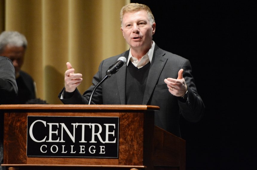 A man speaks into a microphone mounted to a lectern bearing the name Centre College.