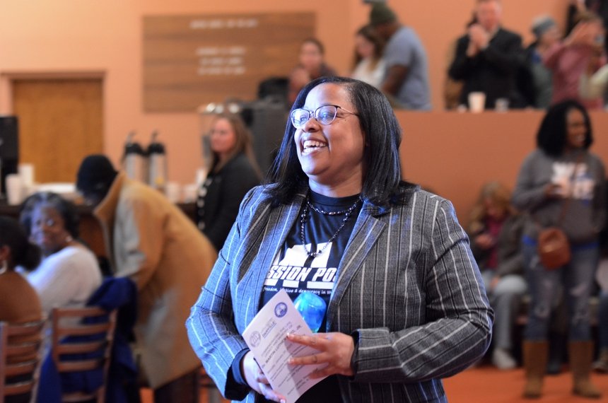 A woman smiles as she crosses the Norton Center for the Arts lobby with a large group of people seen in the background.